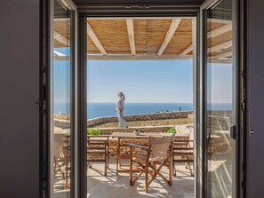A patio with a stone wall, wooden furniture, and a view of the sea. - Moniasma Rustic Stone House in Folegandros (Ano Meria)