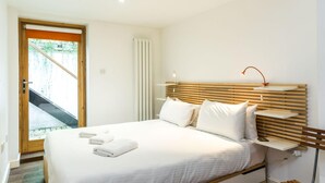 A modern bedroom with a wooden headboard, white bedding, and a bedside table with a lamp. - Charming 2 Bedroom Apartment in Kentish Town (London)