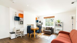 A compact living space with a dining area, a sofa, a bookshelf, and a radiator. - Charming 2 Bedroom Apartment in Kentish Town (London)