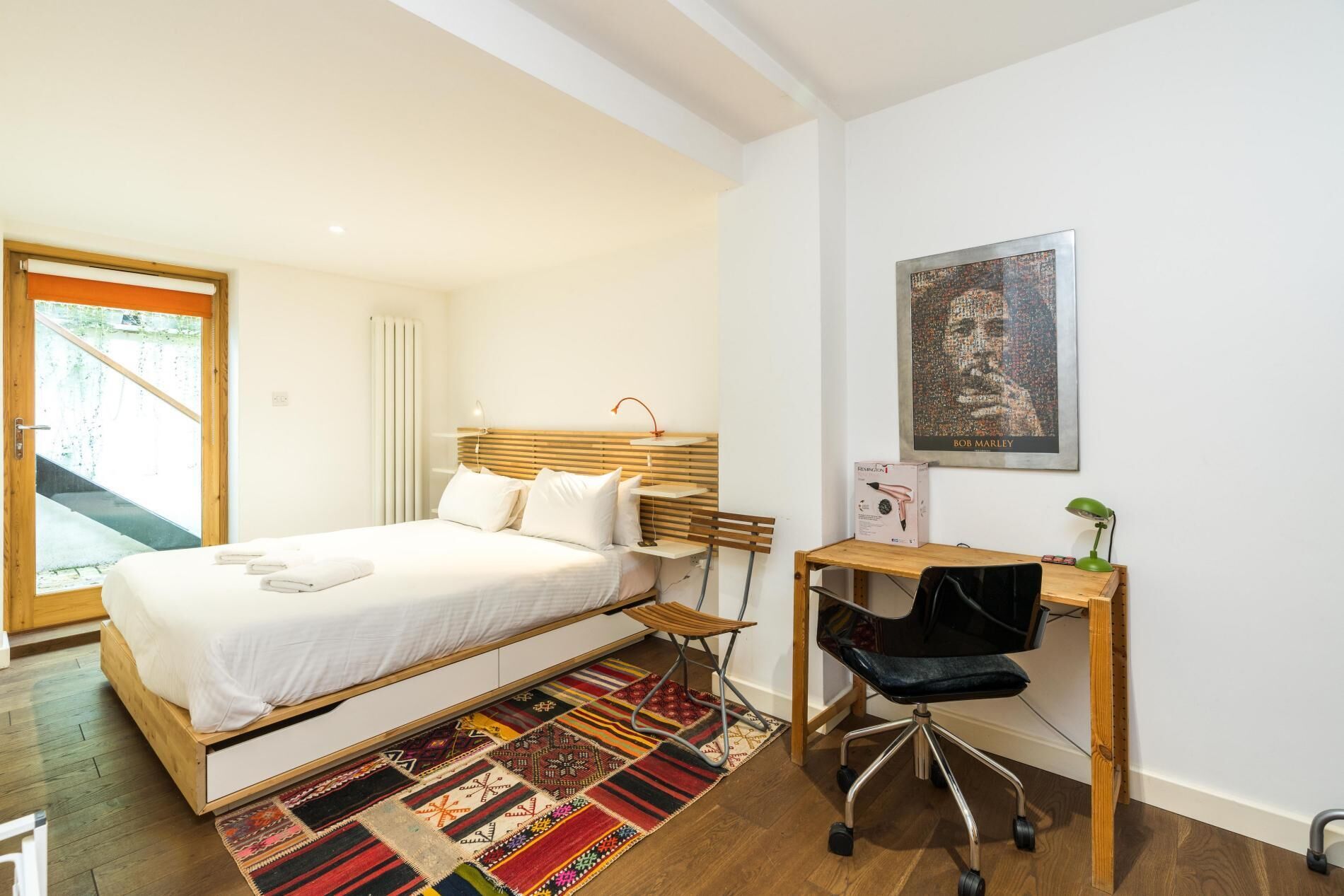 Une chambre à coucher avec un lit, un bureau, une chaise, un radiateur et une affiche accrochée au mur.