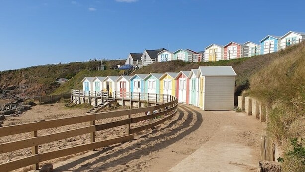 A sandy beach with colorful beach huts and a wooden fence. - Large 3 bed bungalow set in Woodland grounds near Tamar lakes and local beaches (Kilkhampton)
