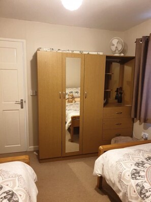 A bedroom with a wardrobe, a bed, a bedside table, a mirror, and a ceiling fan. - Large 3 bed bungalow set in Woodland grounds near Tamar lakes and local beaches (Kilkhampton)