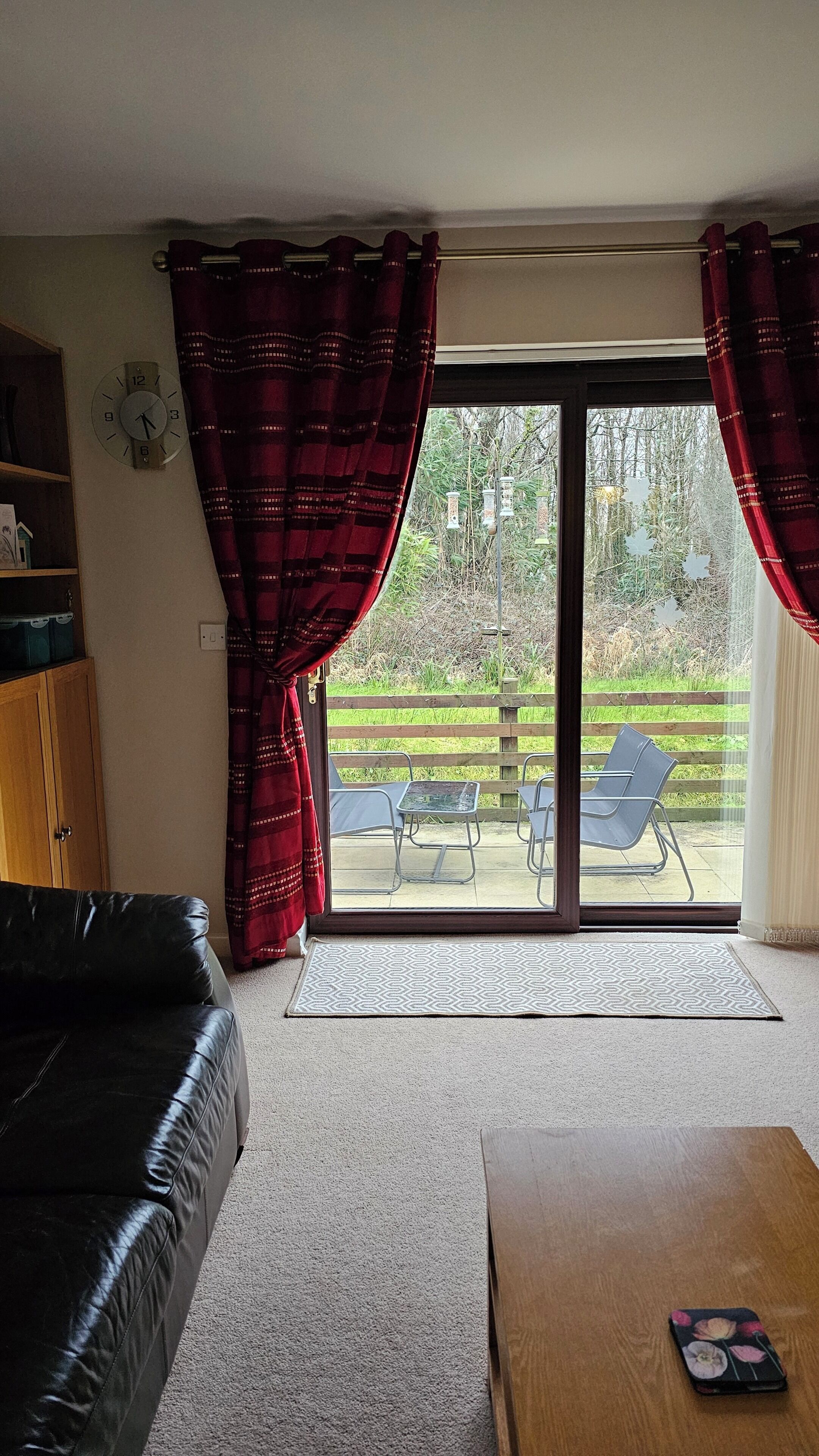 A living room with a black leather sofa, a wooden coffee table, and a sliding glass door leading to an outdoor patio with chairs and a table.