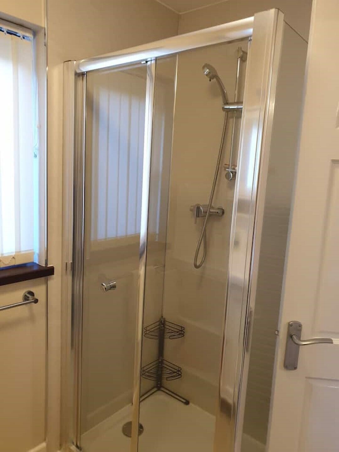 A glass-enclosed shower stall with a handheld showerhead and a corner rack.