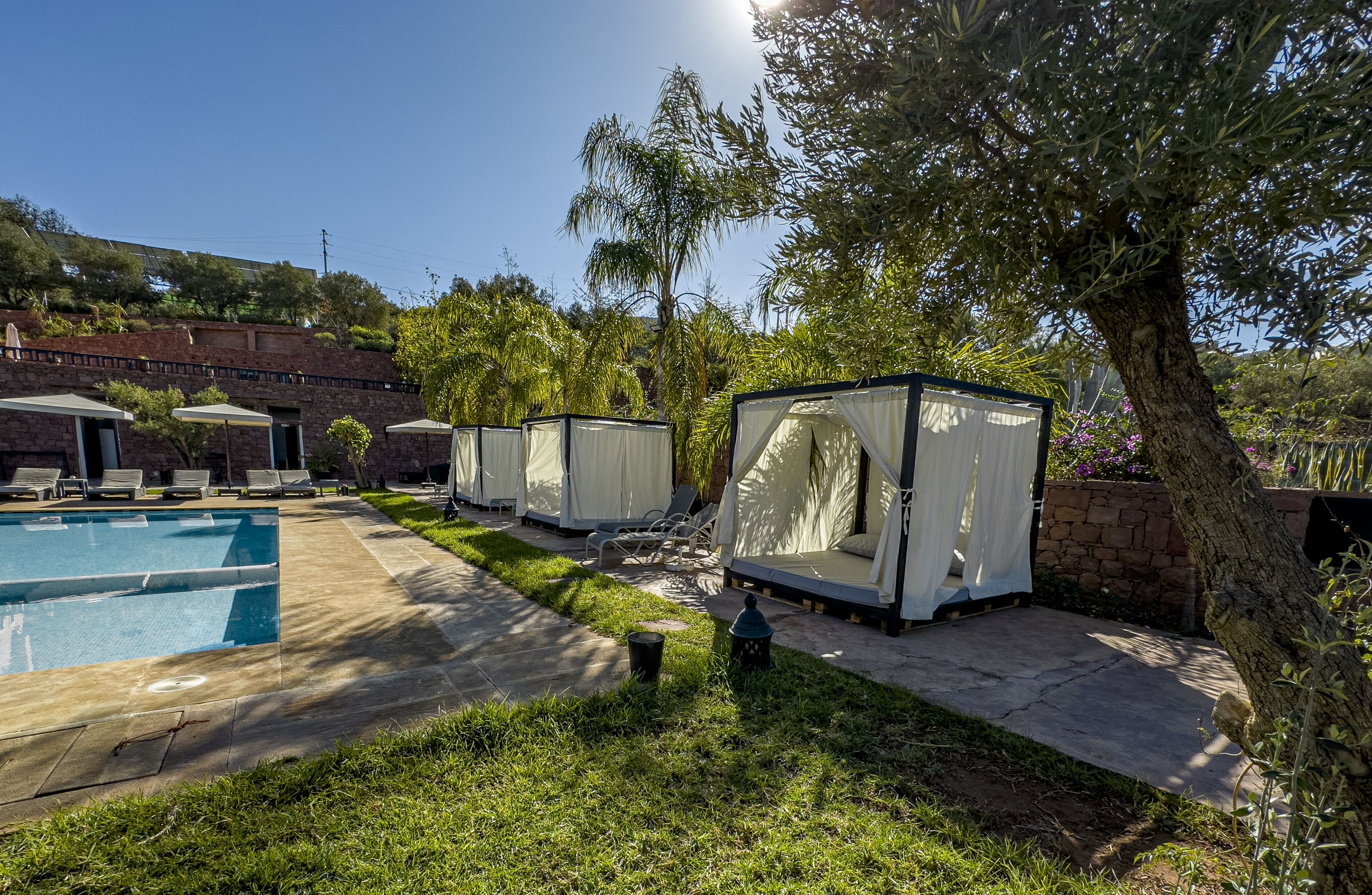 Uma área à beira da piscina com espreguiçadeiras e uma piscina. Há vários espaços de estar cobertos com cortinas.