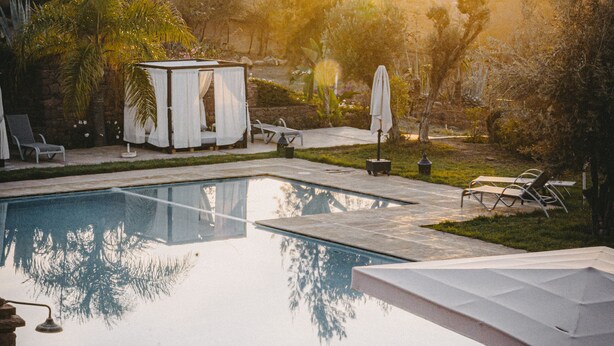 A swimming pool with lounge chairs, a covered seating area, and a view of hills in the background. - Kasbah Agounsane (Ourika)