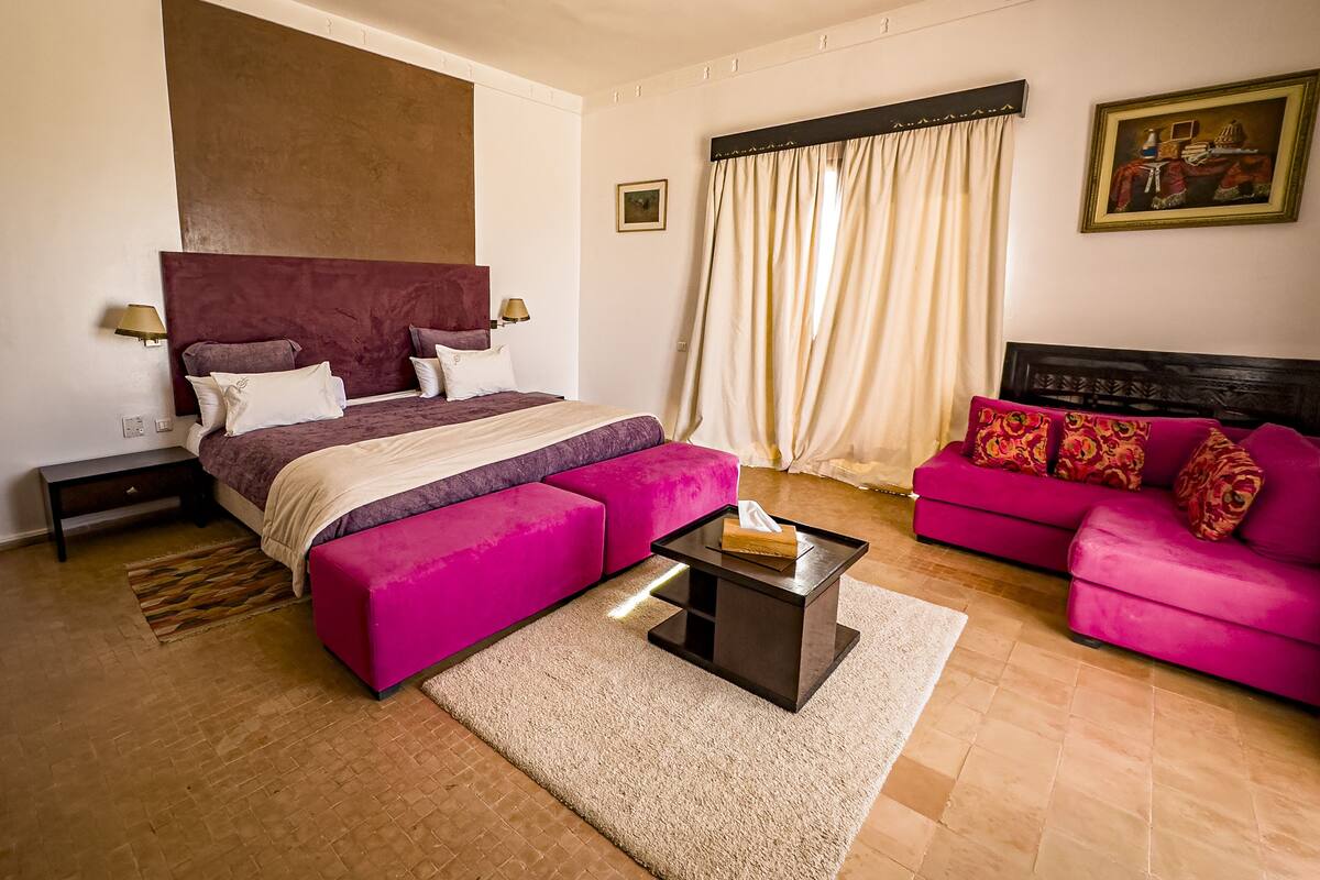 A bedroom with a large bed, a sofa, a nightstand, and a bedside table.