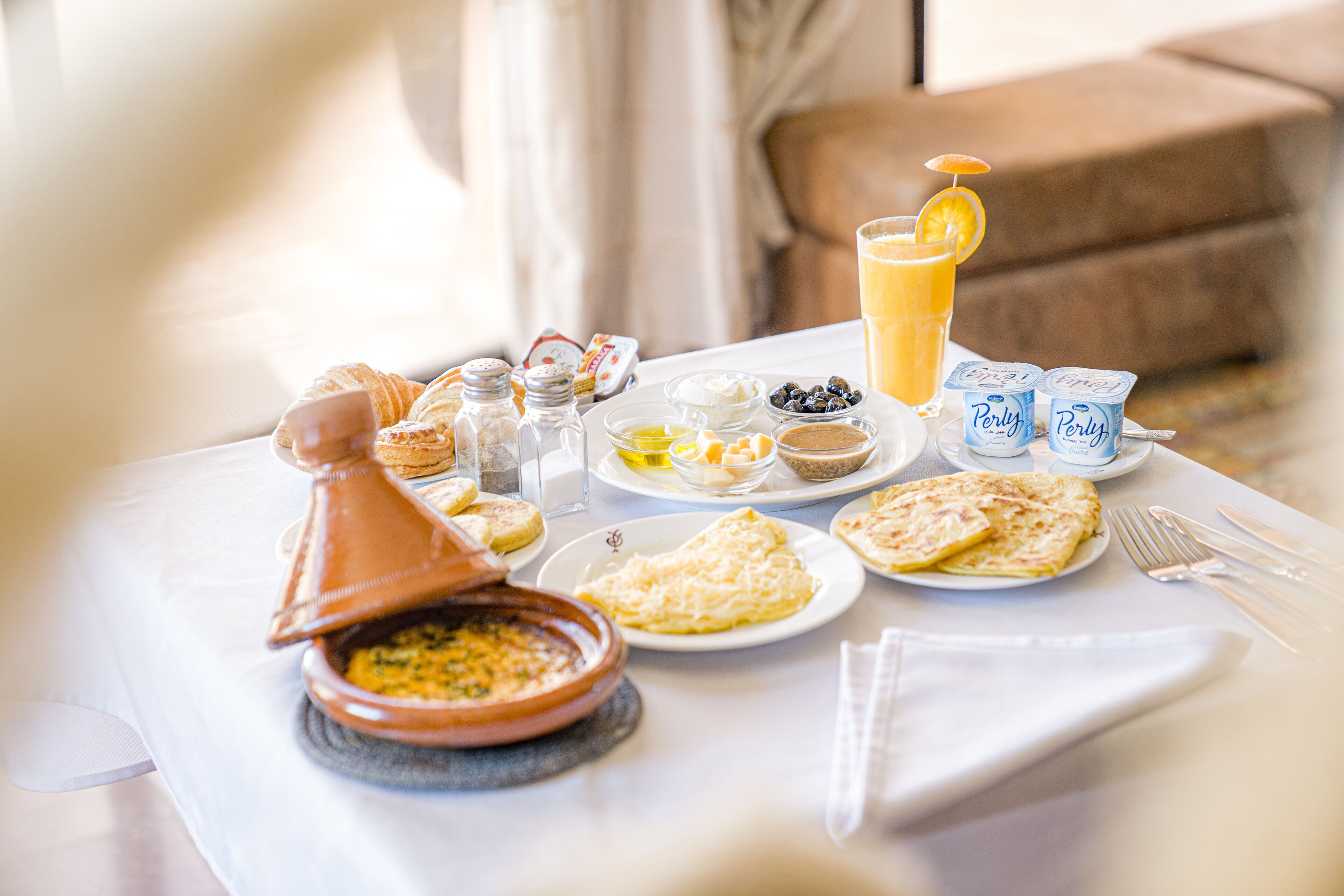 A breakfast table with various dishes, including croissants, a bowl of soup, and a glass of orange juice.
