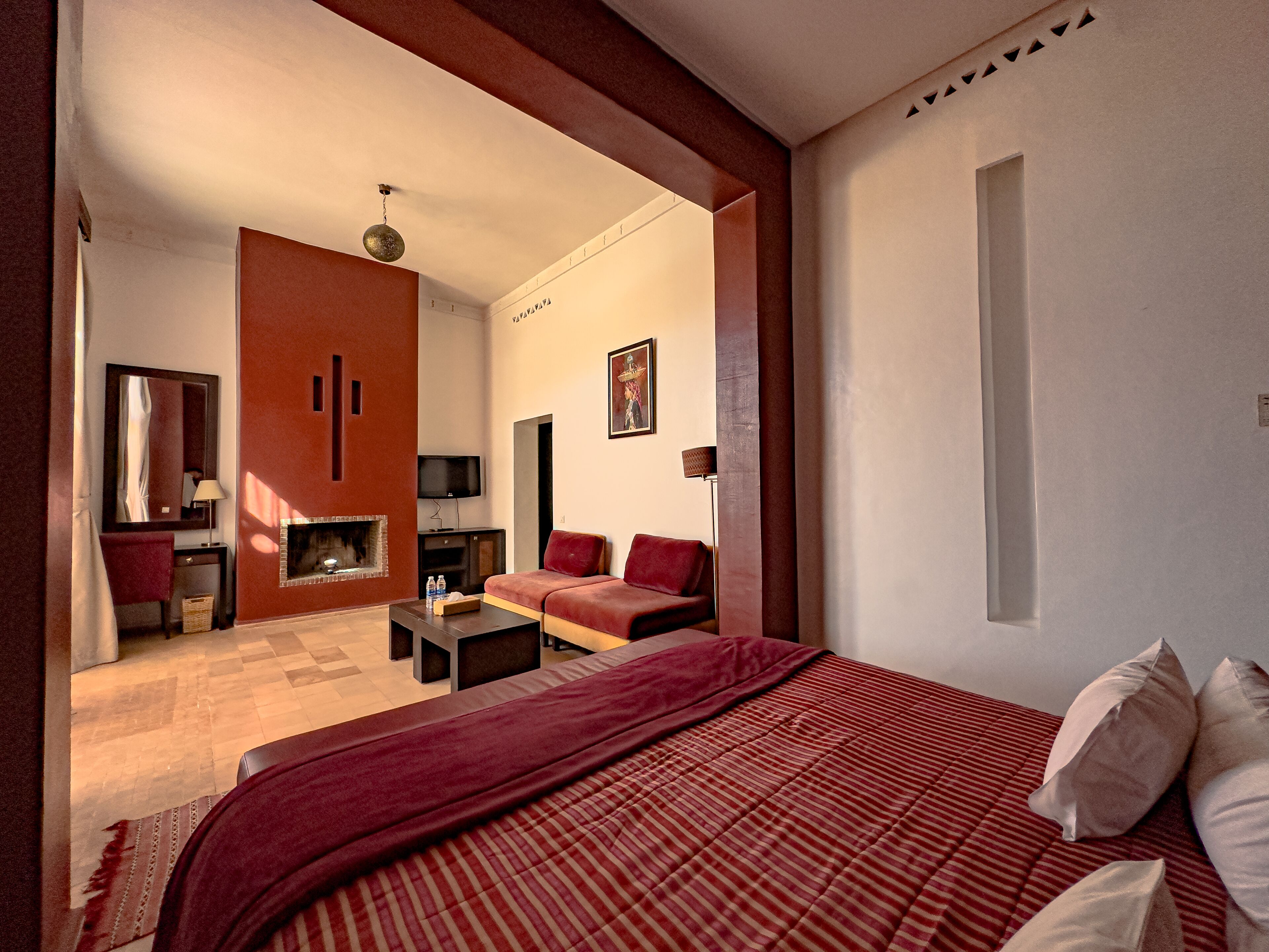 A modern hotel room with a large bed, a sofa, a TV, and a fireplace.