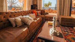 A cozy living room with a brown sofa, a coffee table, and a view of the outdoors. - Kasbah Agounsane (Ourika)