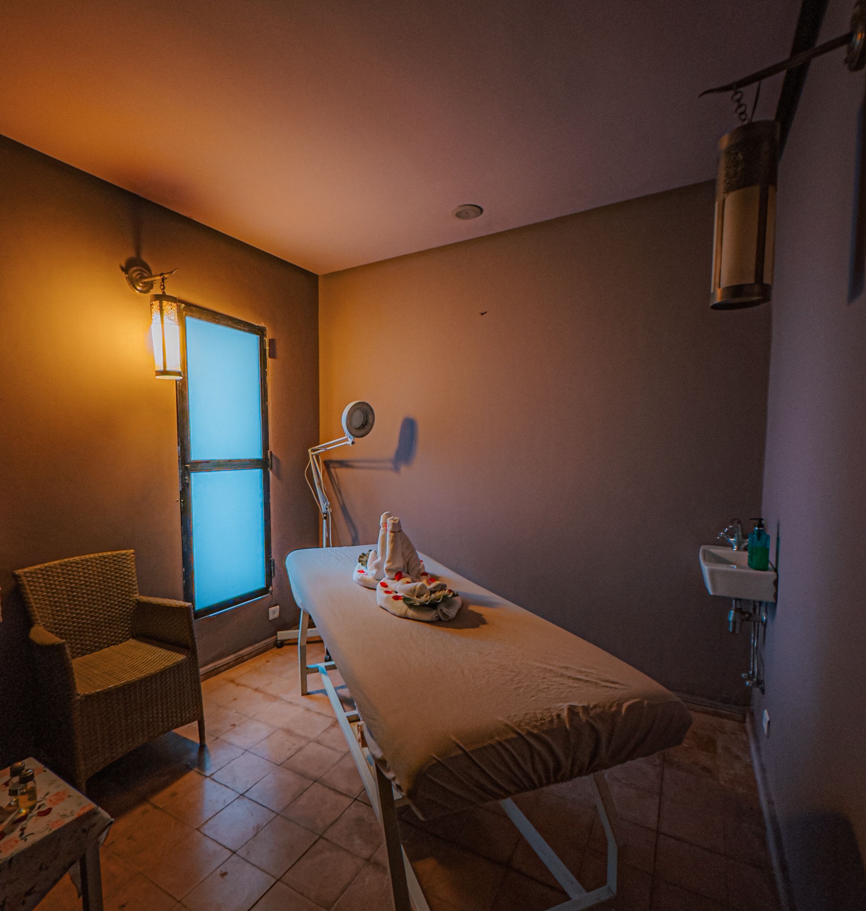 Una habitación con una cama, una silla, un ventanal, un lavamanos y una lámpara.