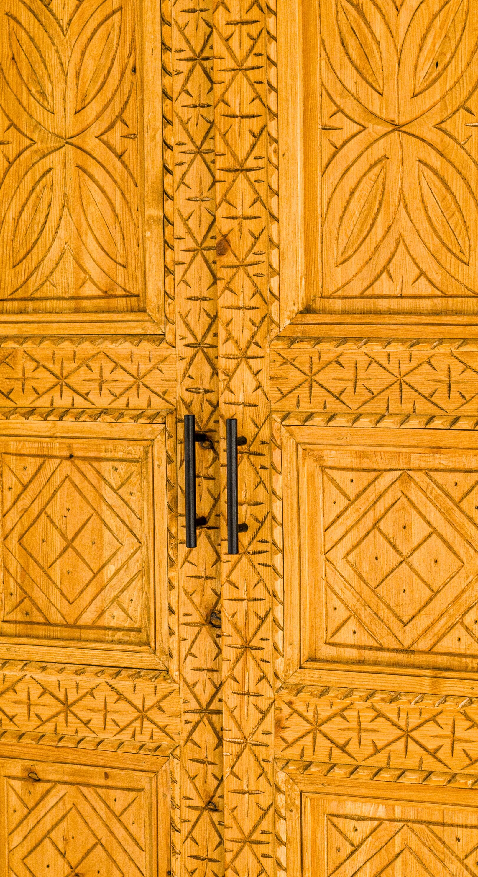 Een houten deur met gedetailleerde geometrische decoraties en twee zwarte handgrepen.