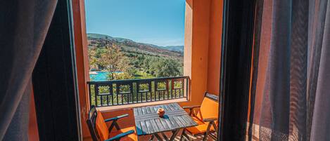A balcony with a table and chairs, a pool in the background, and a view of the countryside.