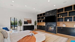 Ein modernes Schlafzimmer mit einem großen Bett, Einbauschränken, einem Kamin und einem an der Wand montierten Fernseher.