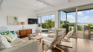 Una sala de estar moderna con sofá, sillones, televisor y vistas al exterior.
