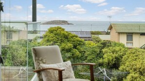 Un balcón con una silla, un tendedero y vista a una isla y al mar en la distancia.