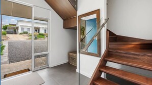 Un interior moderno con una escalera de madera, un vidrio corredero que da al exterior y vista a una zona residencial.