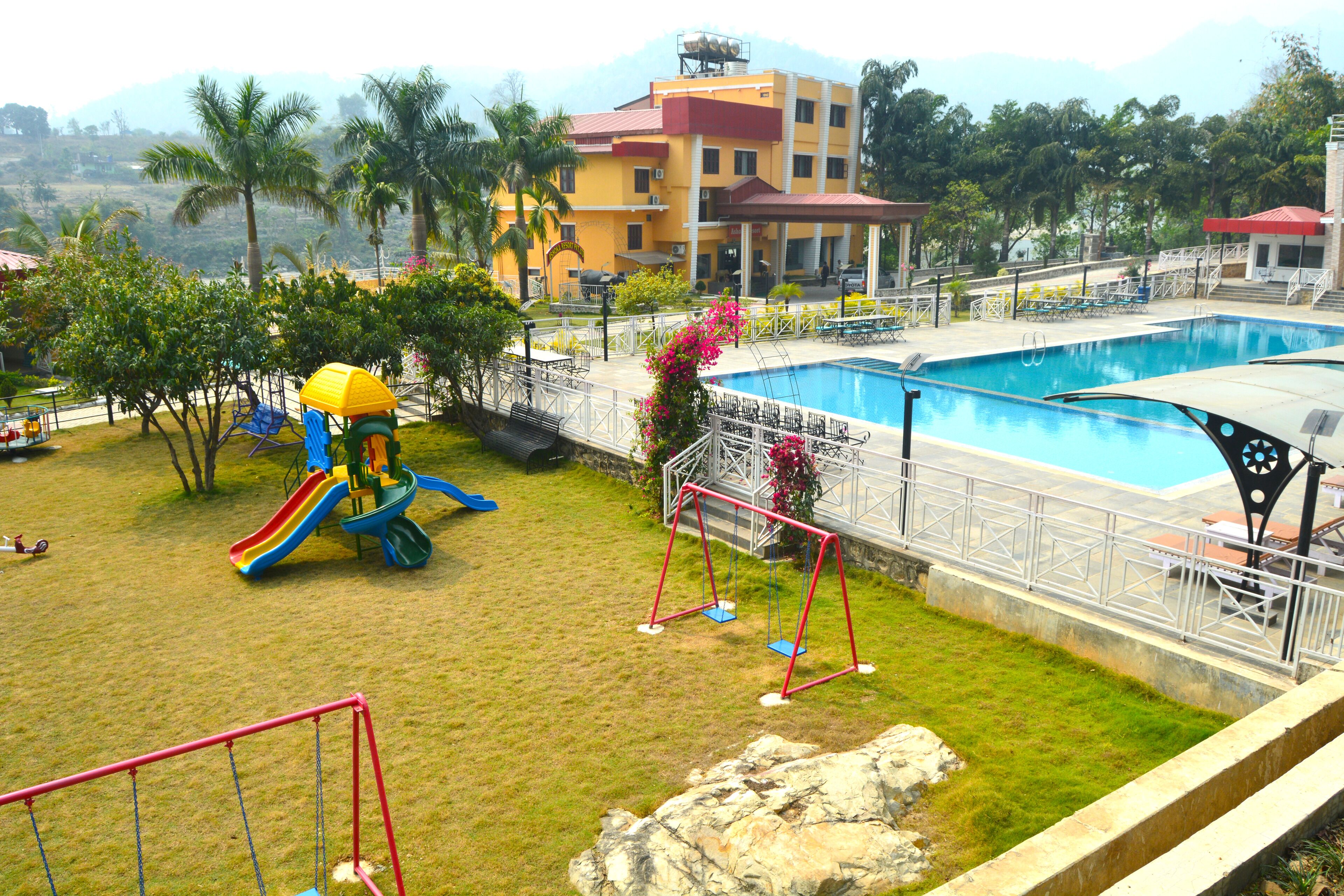 A playground with slides and swings, a swimming pool, and a building with a red roof in the background.