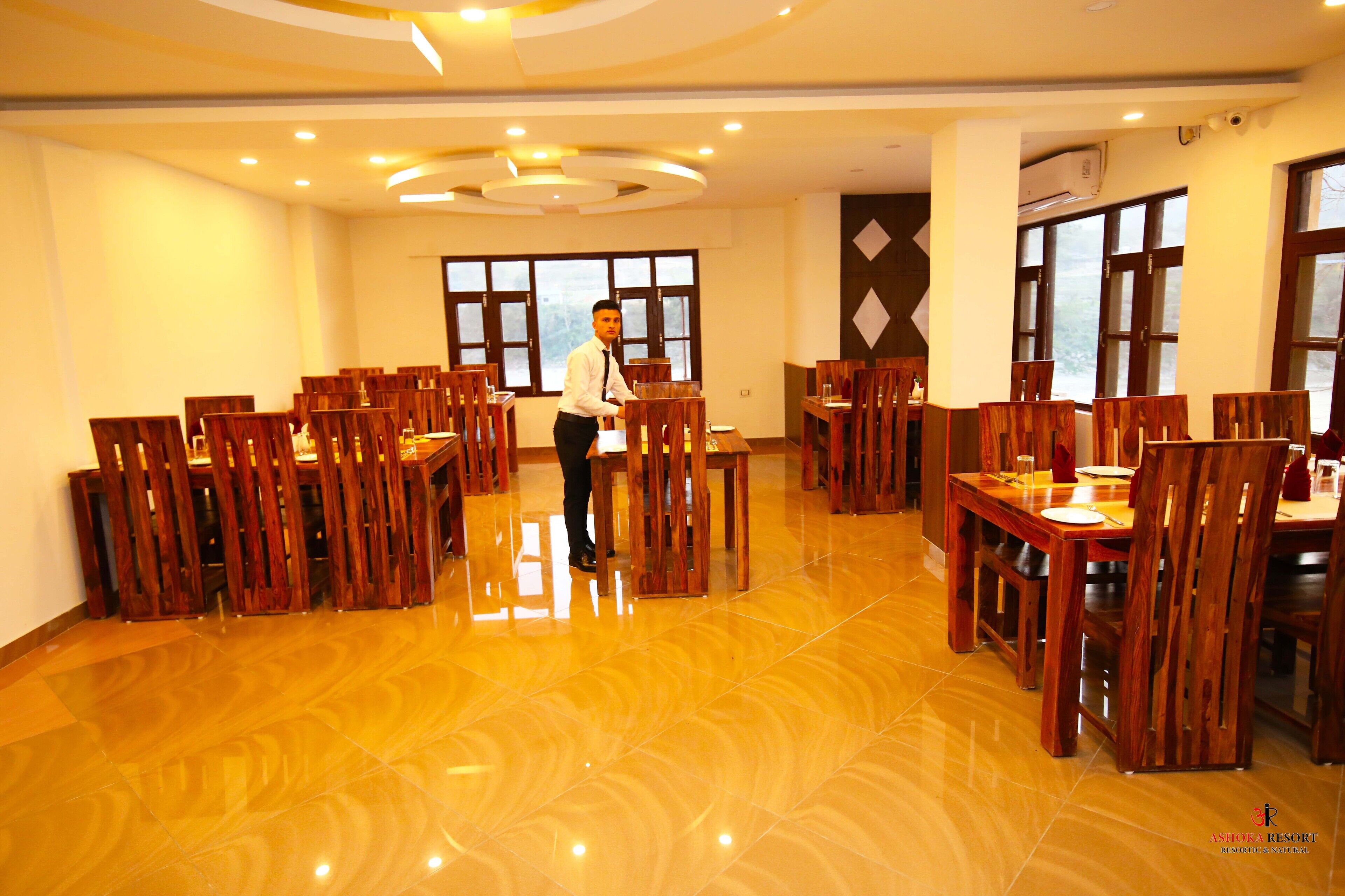 A spacious dining area with wooden tables and chairs, a polished floor, and large windows allowing natural light.