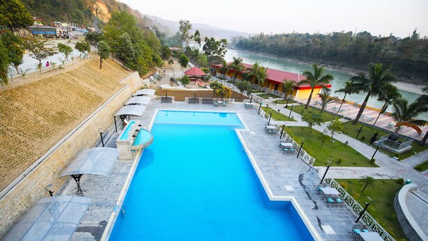 A large swimming pool with a surrounding patio area, a view of the river, and a mountainous backdrop. - Ashoka Resort Pvt. Ltd (Kabilas)