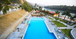 A large swimming pool with a surrounding patio area, a view of the river, and a mountainous backdrop. - Ashoka Resort Pvt. Ltd (Kabilas)