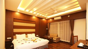 A hotel room with a large bed, a desk, a chair, a TV, and a window with curtains. - Ashoka Resort Pvt. Ltd (Kabilas)