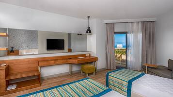 Habitación de hotel con una cama grande, un escritorio con televisor, una mesita y vista a la playa.