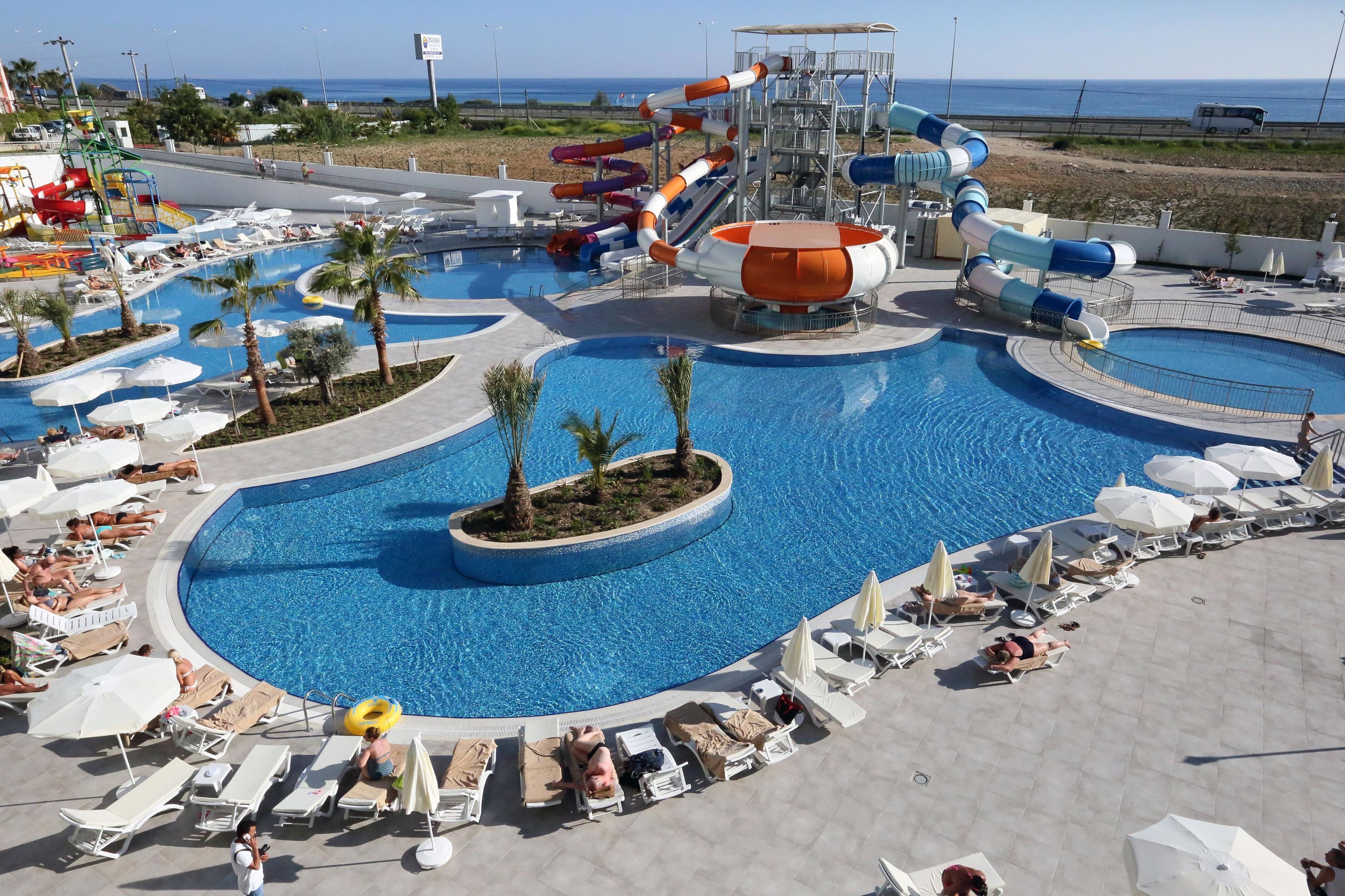 Ein Poolbereich einer Ferienanlage mit mehreren Wasserrutschen und Liegestühlen.
