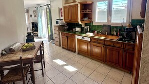 A kitchen with wooden cabinets, a dining table, chairs, a microwave, and a window with curtains. - Pretty villa with private pool (Valréas)