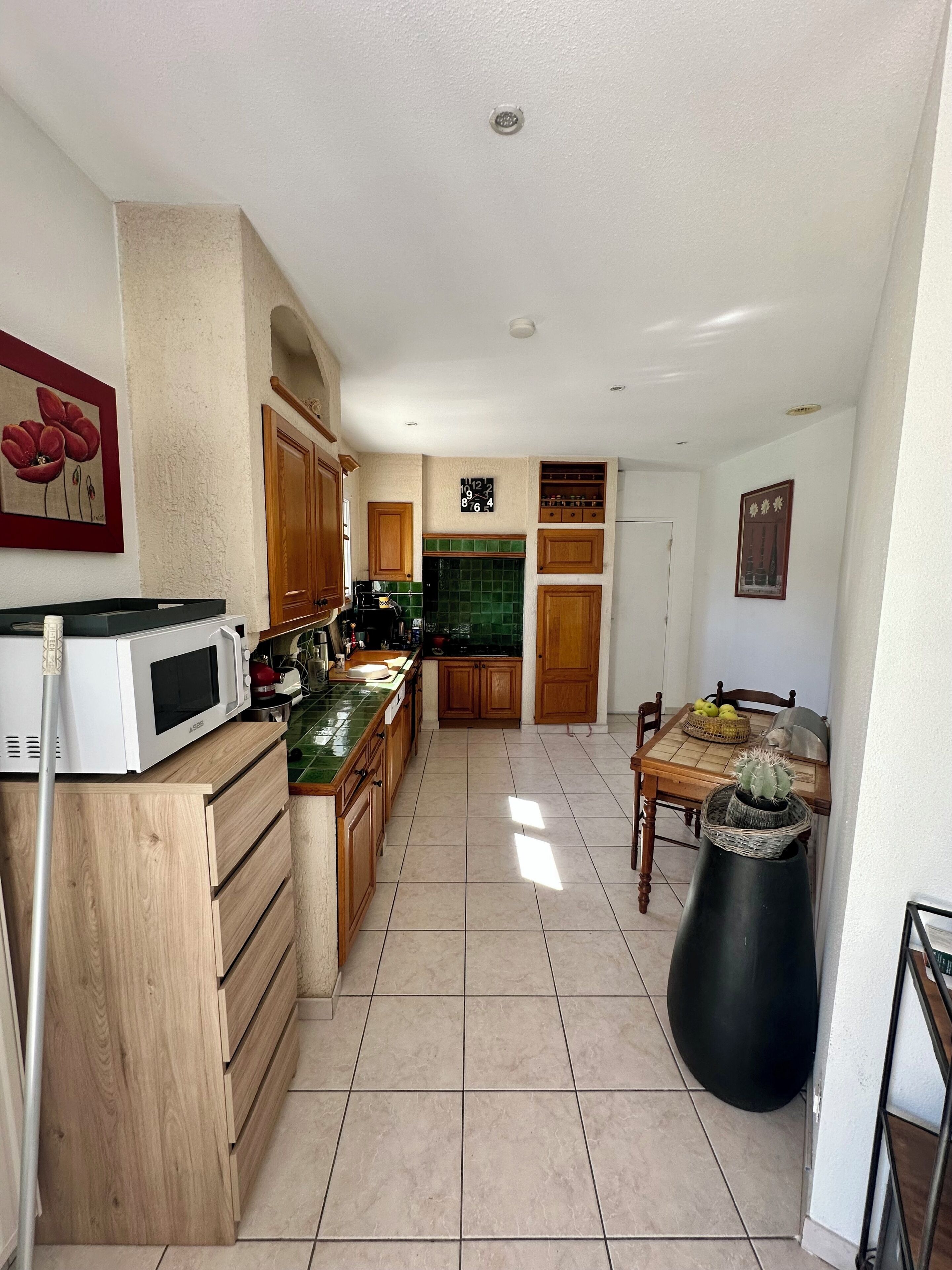 A kitchen with wooden cabinets, a microwave, a clock, and a dining table with a cactus.
