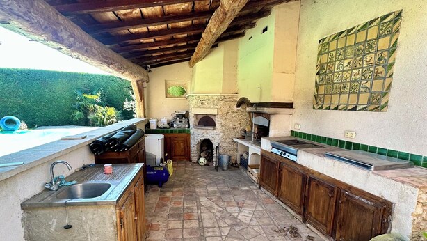 An outdoor kitchen with stone flooring, wooden cabinets, and a stone fireplace. - Pretty villa with private pool (Valréas)