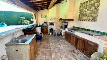 Une cuisine extérieure dotée d’un sol en pierre, de meubles en bois et d’une cheminée en pierre.