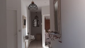 A narrow hallway with a white door on the left, a small table with a decorative bowl, and a mirror with leaf patterns on the right. - Pretty villa with private pool (Valréas)