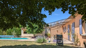 A backyard with a swimming pool, a covered patio, and a garden area with various plants. - Pretty villa with private pool (Valréas)