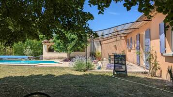 Un jardin avec une piscine, un patio couvert et un espace aménagé avec différentes plantes.