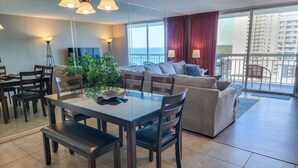 A modern living room with a dining area, large windows, and a balcony. - 1201 South Hampton 2 Bedroom Condo (Myrtle Beach)