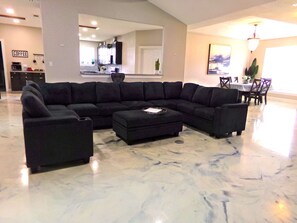 A living room with a sectional sofa, a dining area with a table and chairs, and a kitchen in the background.