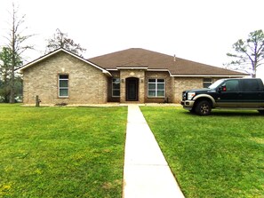 A two-story house with a brick facade, a front entrance, and a driveway leading to a parked truck. - Bayou, Blues & Views (Pensacola)