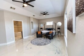 A bedroom with a bed, two chairs, a round rug, two bedside tables, a ceiling fan, and a bathroom with a bathtub. - Bayou, Blues & Views (Pensacola)