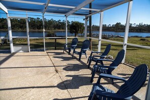 A covered outdoor seating area with chairs and a table, overlooking a lake and trees. - Bayou, Blues & Views (Pensacola)