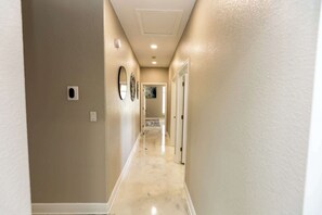 Een gang met beige wanden, een marmeren vloer en een plafond met inbouwverlichting.