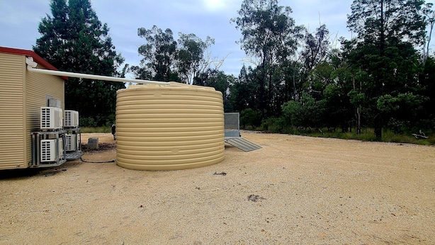 A building with a beige exterior, air conditioning units, and a large cylindrical tank. - Bush getaway -technology free, soaking up the Aussie Bush (Crossroads)