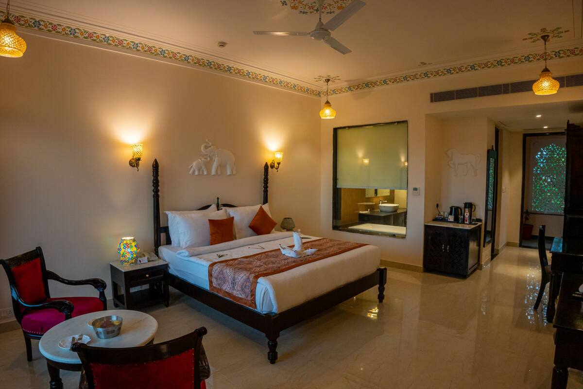 A hotel room with a bed, a chair, a small table, a nightstand, and a mirror.