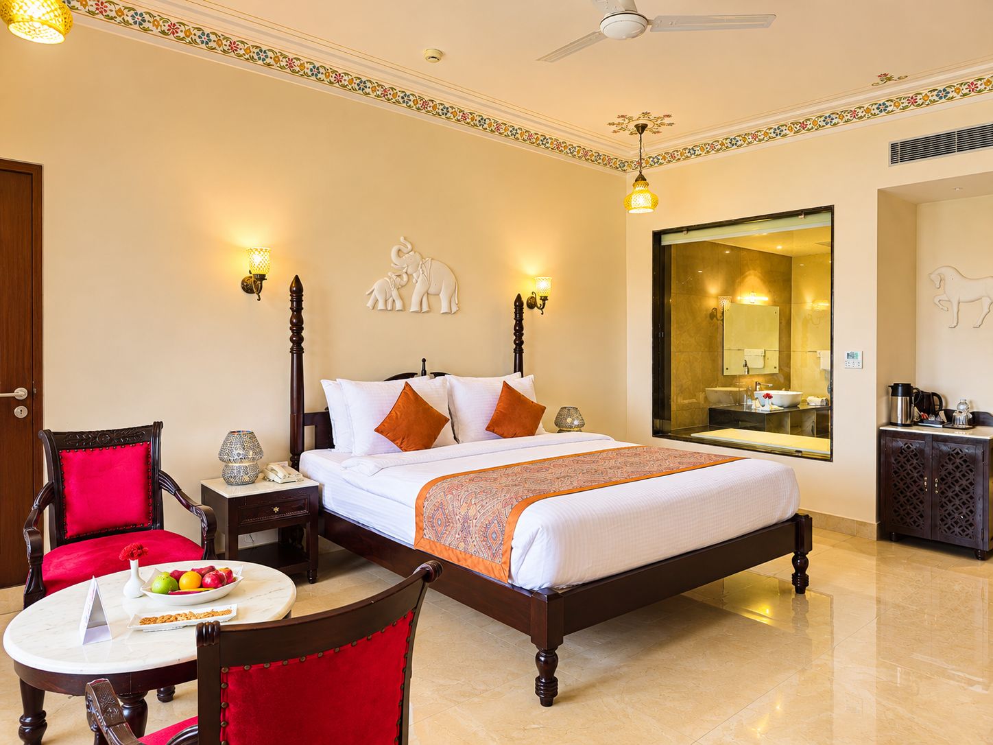 A hotel room with a bed, a sitting area with a table and chairs, a decorative wall piece, and a large mirror.