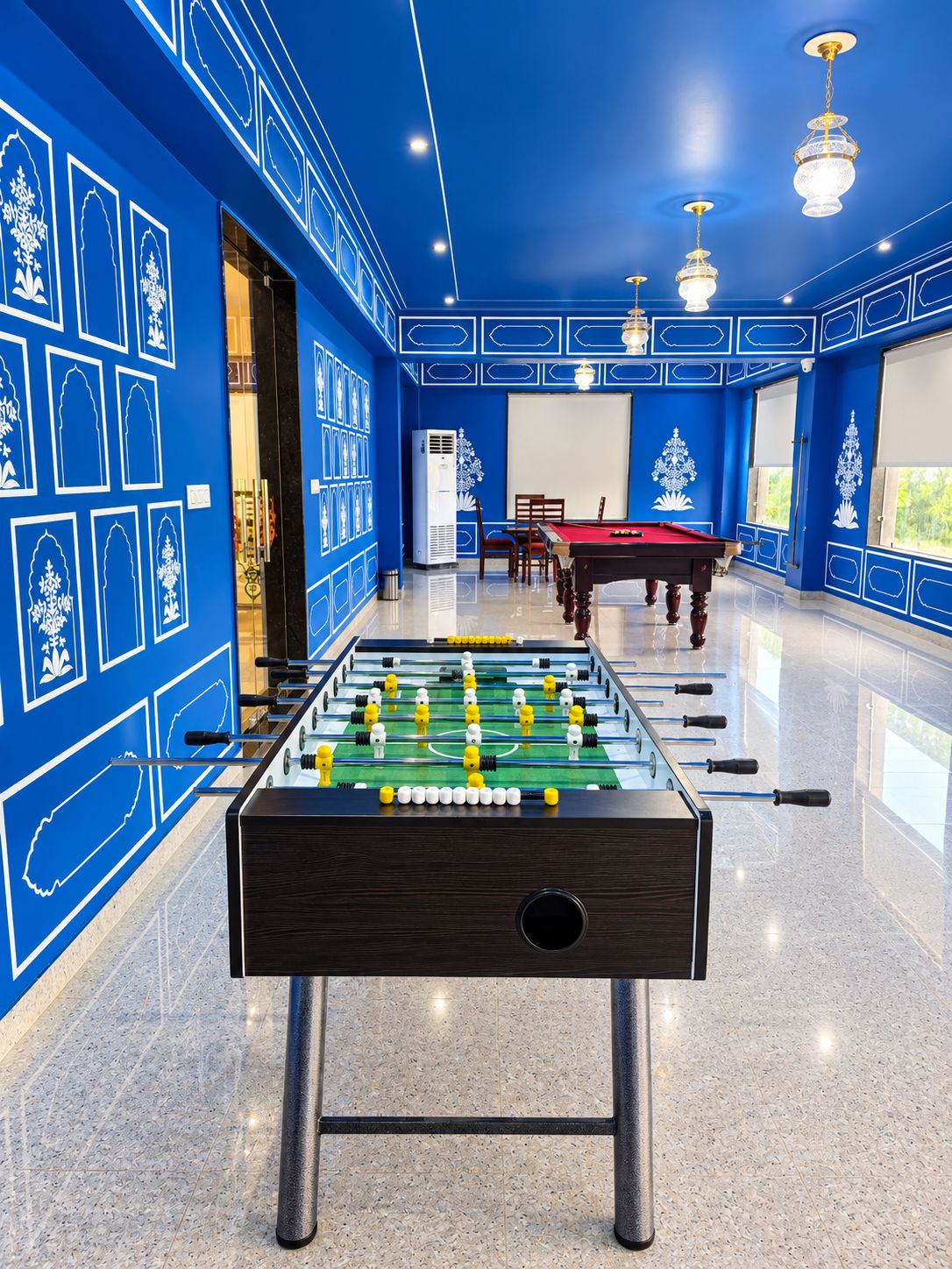 A room with a foosball table, a pool table, and a billiards table.