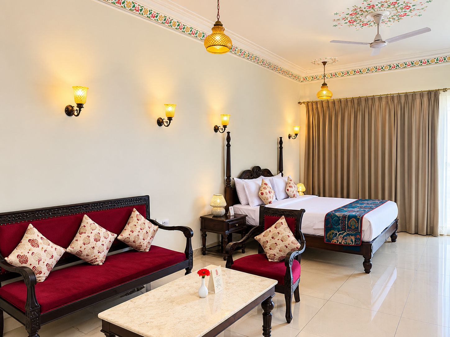 A hotel room with a bed, a sofa, a table, and wall-mounted lamps.