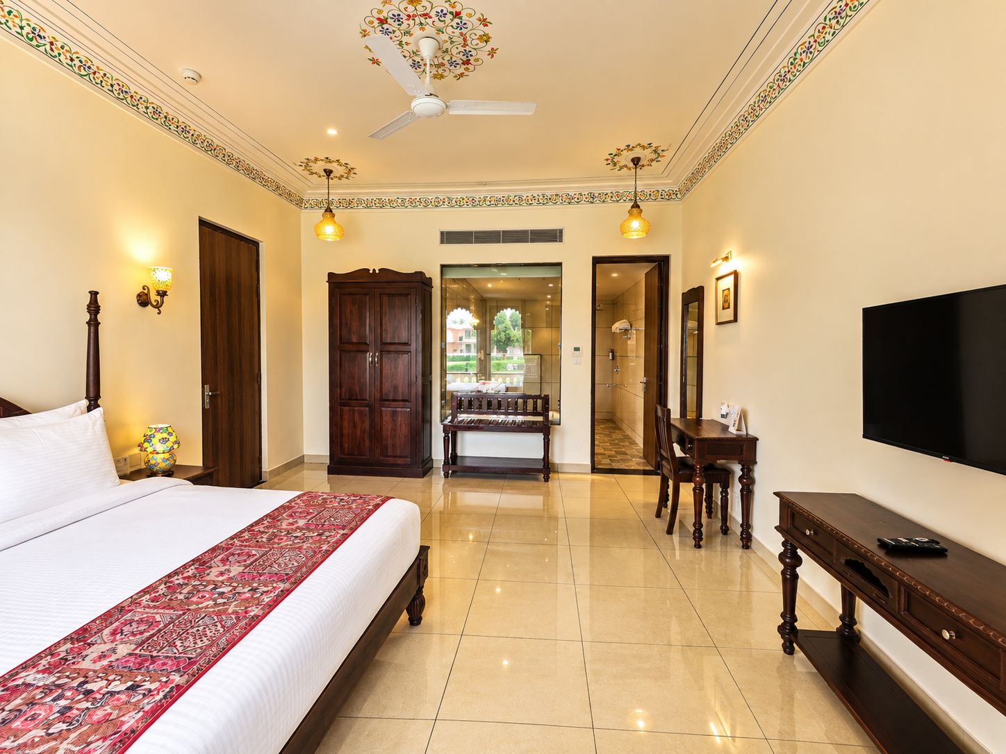 A hotel room with a bed, a desk, a television, and a bathroom visible through an open door.