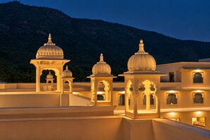 A traditional building with multiple domed structures and ornate arches, set against a mountainous backdrop.