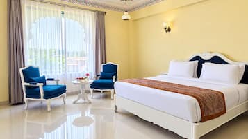 A hotel room with a large bed, two blue armchairs, a small table, and a window with curtains.