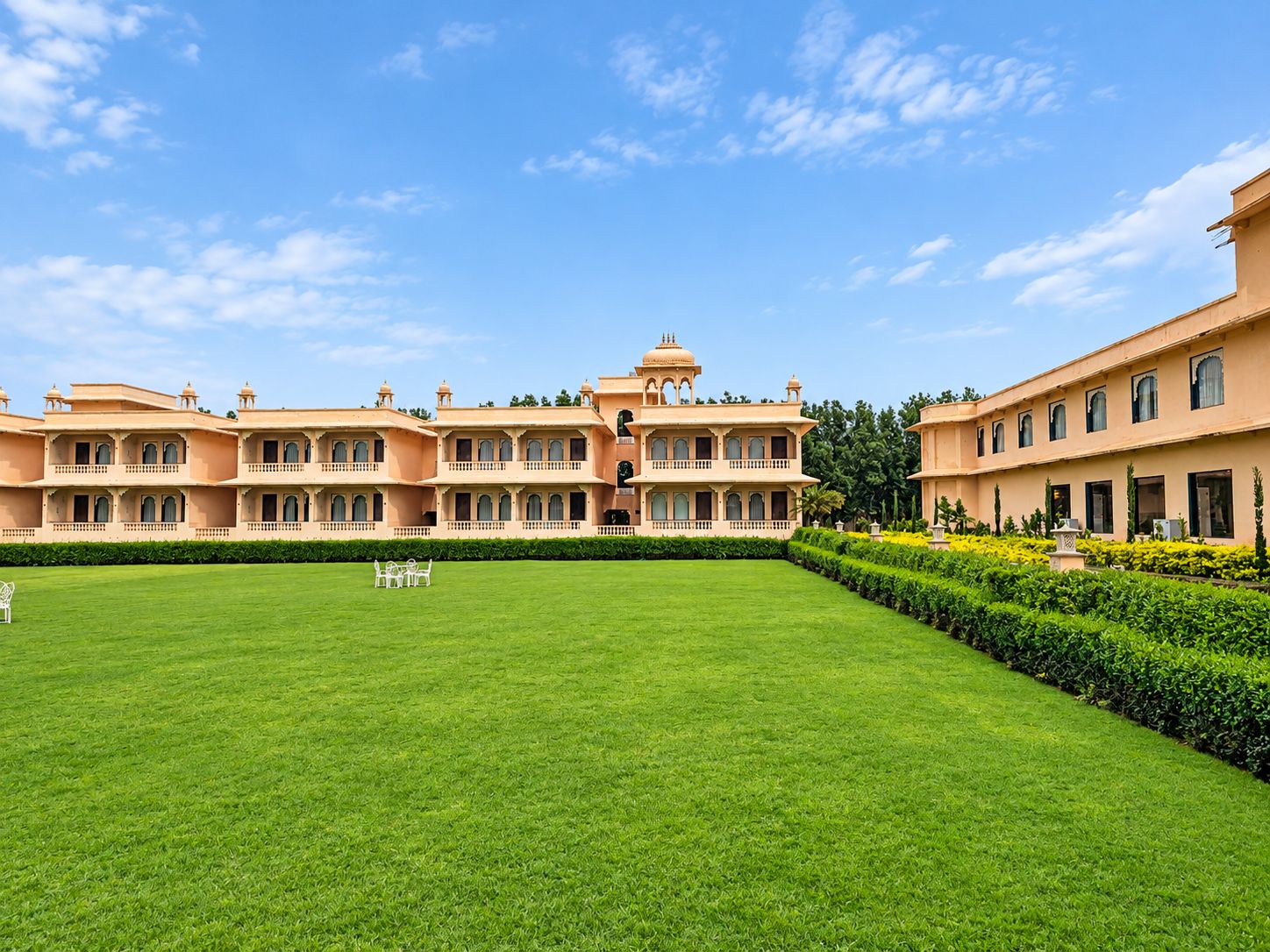 A large, multi-story building with a symmetrical facade, a central courtyard with a lawn, and a clear blue sky.